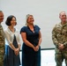 Four individuals pose together in what appears to be an indoor military or official setting. Two are wearing U.S. Army combat uniforms (OCP pattern) and two are in civilian attire. The group appears to be at a formal or ceremonial event, smiling for the photo.