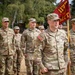 A group of U.S. Army soldiers in MultiCam/OCP camouflage uniforms are assembled outdoors, likely during a military ceremony or formation. The central figure, identified by name tape as 'MCNEIL,' holds a red unit guidon bearing the designation '117 MCT.' Soldiers in the background include individuals identified as 'PEREZ' and 'STEELE,' with various ranks visible including a Captain's rank insignia on MCNEIL.