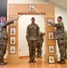 A U.S. Army NCO induction or promotion ceremony is taking place indoors. Two soldiers in OCP (Operational Camouflage Pattern) uniforms hold crossed sabers over a third soldier standing beneath a decorative wooden arch displaying NCO rank insignia. A unit patch featuring a horse (likely 1st Cavalry or similar) is visible on the floor in a frame.