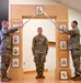 A U.S. Army promotion or graduation ceremony is taking place indoors, featuring a ceremonial arch with NCO rank insignia plaques. Two soldiers in OCP (Operational Camouflage Pattern) uniforms cross sabers/swords over a third soldier standing at attention beneath the arch. The ceremony appears to be an NCO induction or promotion ceremony, likely associated with the Pennsylvania National Guard based on visible unit insignia.