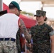A U.S. Marine in MARPAT digital camouflage uniform is shaking hands with a military personnel wearing a green beret and multicam trousers with a white athletic shirt, suggesting an awards or recognition ceremony. The event appears to be a large public military gathering with a significant crowd visible in the background. Multiple service members from different branches or nations are present, indicating a joint or multinational military event.