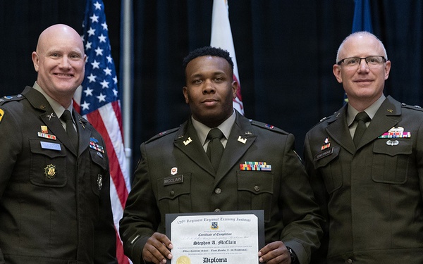 Three U.S. Army soldiers in dress green uniforms pose for a formal photo at what appears to be a military graduation or commissioning ceremony. The center soldier, identified by his name tape as 'McClain,' holds a diploma/certificate of completion from the 120th Regiment Regional Training Institute for Stephon A. McClain, Officer Candidate School. Two senior officers flank him on either side.