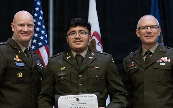 Three individuals in U.S. Army military uniforms pose for a formal photograph at what appears to be a graduation or commissioning ceremony. The person in the center is holding a diploma from the 129th Regiment Regional Training Institute, Certificate of Completion for 'Alexis Rodriguez' from Officer Candidate School. Two senior officers flank the graduate against a backdrop of American and state flags.