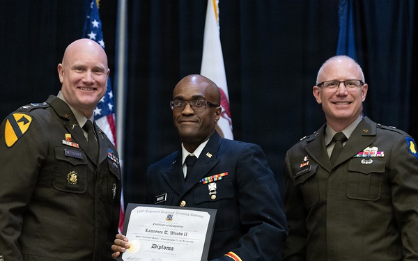Three military personnel pose for a formal photograph during what appears to be a graduation or commissioning ceremony. The central figure, identified by the diploma as Lawrence T. Woods II, holds a Certificate of Completion/Diploma from the 759th Regiment Regional Training Institute. Two officers in Army green service uniforms flank him on either side.