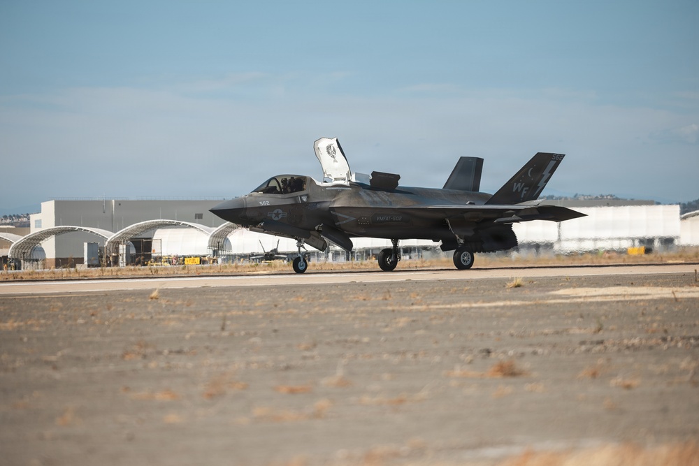 A U.S. Marine Corps F-35B Lightning II stealth fighter jet is taxiing on a runway at a military airbase. The aircraft's canopy is open and it bears tail code 'WF' with the number '562' visible on the fuselage, indicating it belongs to VMFAT-501 or a similar Marine F-35 training squadron. Military hangars and aircraft shelters are visible in the background.
