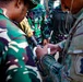 Military personnel from at least two different armed forces are gathered in close proximity, appearing to review notes or documentation. One soldier wears Indonesian Armed Forces (TNI) camouflage and another wears US Army MultiCam (OCP) uniform with a visible unit patch. The interaction suggests a joint training exercise or coordination meeting between allied military forces.