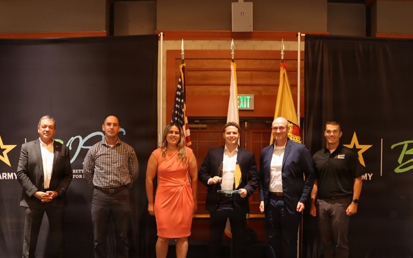 Six individuals are posed on a stage at a U.S. Army BOSS (Better Opportunities for Single Soldiers) event or awards ceremony. One person in the center is holding what appears to be a trophy or award. The backdrop prominently displays the U.S. Army and BOSS program branding.