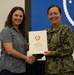 A U.S. Navy officer in NWU Type III camouflage uniform is presenting a certificate to a civilian woman during a formal recognition ceremony. The certificate is awarded to Katherine N. Tice in recognition of fifteen years of service to the Government of the United States of America. Both individuals are smiling and shaking hands while jointly holding the certificate.