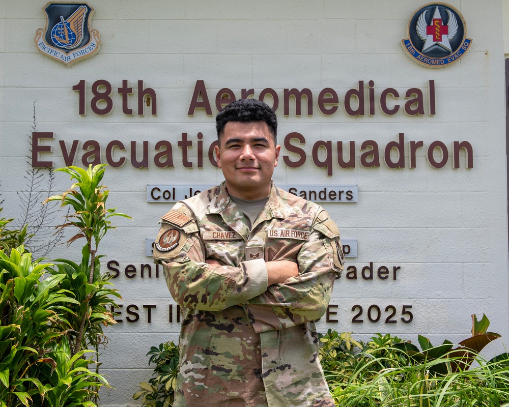 A U.S. Air Force service member named Chavez poses with arms crossed in front of the 18th Aeromedical Evacuation Squadron sign. The individual is wearing OCP (Operational Camouflage Pattern) uniform with visible name tape and U.S. Air Force tape. The photo appears to be an official or semi-official portrait taken outdoors at a military installation.