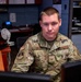 A U.S. Air Force Staff Sergeant named Ward is seated at a desk in an office environment, wearing Operational Camouflage Pattern (OCP) uniform. He is looking directly at the camera with a neutral expression. The setting appears to be a military administrative or medical support office.
