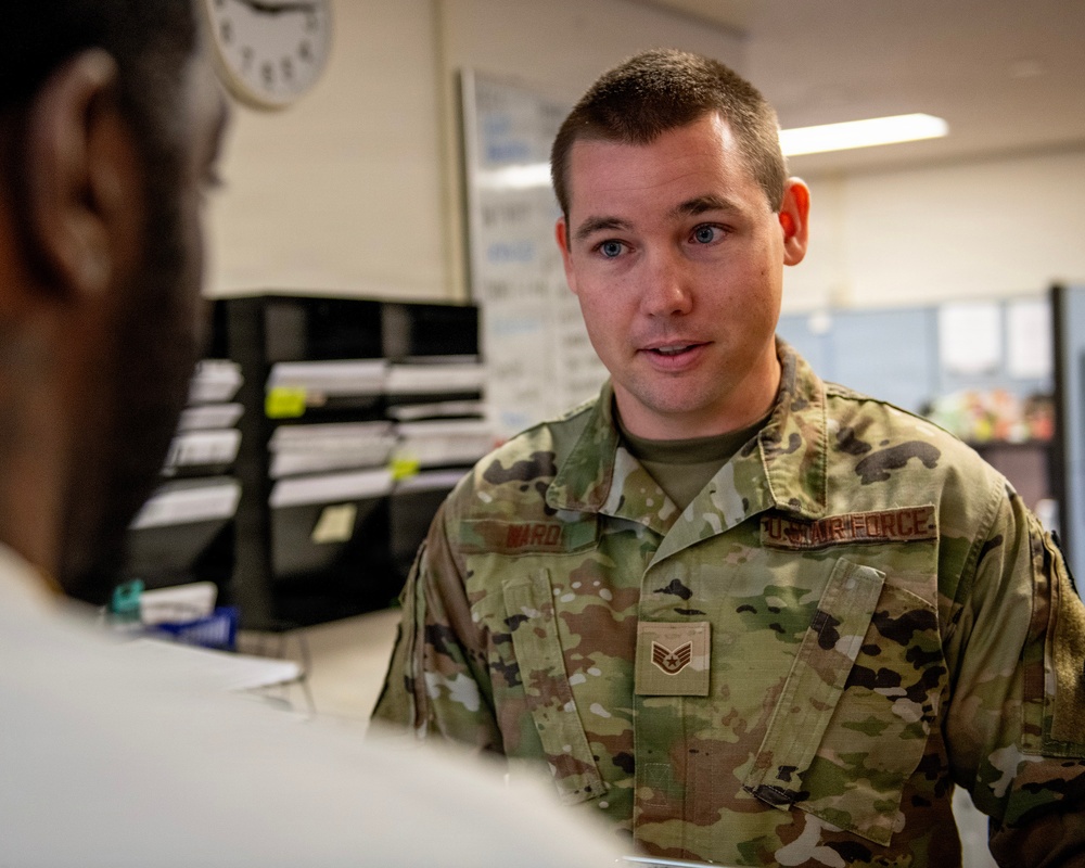 A U.S. Air Force Staff Sergeant wearing OCP (Operational Camouflage Pattern) uniform is engaged in a conversation with another individual whose back is to the camera. The name tape reads 'WARD' and the rank insignia indicates Staff Sergeant. The setting appears to be an administrative or office environment on a military installation.