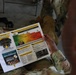 A soldier in camouflage uniform is reading a SHARP (Sexual Harassment/Assault Response and Prevention) Reference Card. The document appears to be an official U.S. Army training material covering prevention, risk reduction, bystander intervention, and related topics. The image is taken from an over-the-shoulder perspective during what appears to be a training or briefing session.