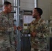 Two U.S. Army soldiers in OCP (Operational Camouflage Pattern) uniforms are engaged in a fist bump greeting inside what appears to be a military facility. The soldier on the left has a name tape reading 'GREBERRY' and the soldier on the right has a name tape reading 'GLOVER', with a SETAF-AF (U.S. Army Africa) patch visible on his right shoulder. The interaction appears friendly and informal.