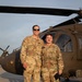 Two U.S. Army soldiers in Operational Camouflage Pattern (OCP) uniforms are posing together on a flight line in front of a UH-60 Black Hawk helicopter. Name tapes visible on their uniforms read 'TREXLER' (left) and 'WARREN' (right), both bearing 'U.S. ARMY' tape. The photo appears to be taken during golden hour lighting at a military airfield.