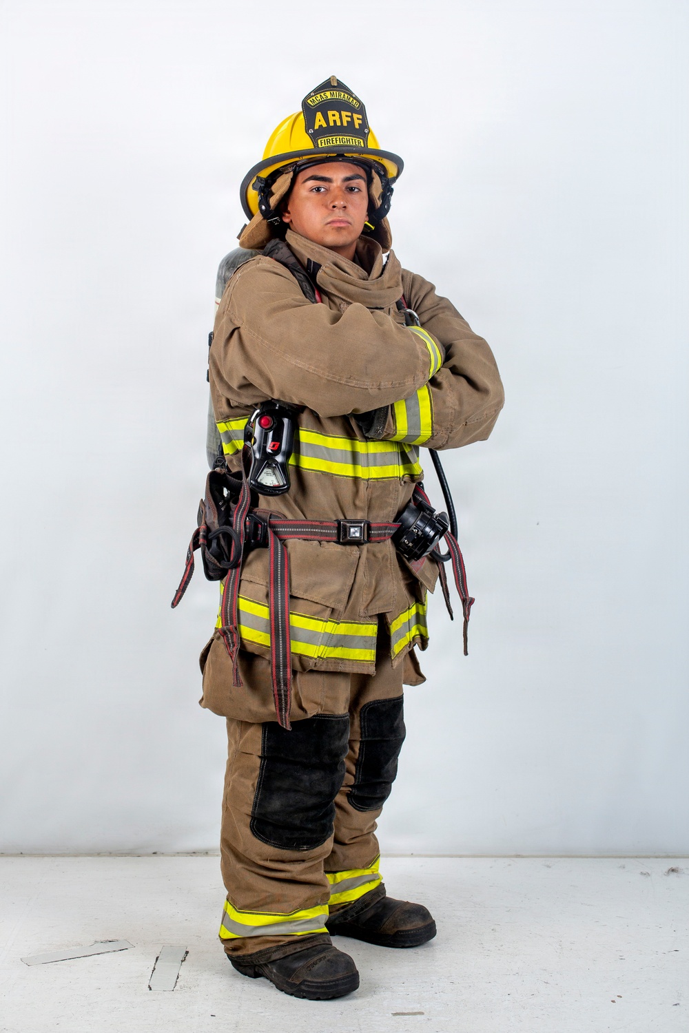 A firefighter in full turnout gear stands posed with arms crossed against a plain white background. The helmet displays 'ARFF' and 'FIREFIGHTER' markings, along with 'MCAS MIRAMAR', identifying this as an Aircraft Rescue and Firefighting specialist from Marine Corps Air Station Miramar. The image appears to be a professional portrait or official photograph.