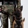 MCAS Marines pose for content 2026 A military or law enforcement working dog, identified as a Belgian Malinois, stands beside a handler wearing MARPAT (Marine Pattern) digital camouflage uniform and tan combat boots. The dog is equipped with a black tactical harness and leash, and is looking directly at the camera in an alert, composed posture. The image appears to be a formal or portrait-style photograph taken against a plain light background.