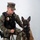 MCAS Marines pose for content 2026 A U.S. Marine Corps Military Police Sergeant, identified by name tape as 'Fesenmaier M.', poses in a studio-style portrait with a Belgian Malinois K9 partner. The Marine is wearing MARPAT digital camouflage utilities, a tactical vest with a gold law enforcement badge, and holds the dog's leash. The K9 is fitted with a black tactical harness and sits attentively beside the handler.