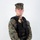 MCAS Marines pose for content 2026 A male service member in U.S. Marine Corps MARPAT woodland digital camouflage uniform is posed against a white studio background. He is wearing a black tactical vest with a law enforcement badge, name tape reading 'FESENMAIER M.', a body camera, and an Eagle Globe and Anchor emblem. He is equipped with a sidearm in a holster on his left hip and appears to be a U.S. Marine Corps Military Police officer.