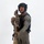 MCAS Marines pose for content 2026 A person in full tactical law enforcement or military-style gear is posed against a plain white background in what appears to be a professional portrait or equipment showcase photo. They are equipped with a large precision rifle with a suppressor and scope, wearing a tactical vest, ballistic helmet with communications equipment, and olive drab uniform. A green patch on the right sleeve reads 'SRT' (Special Response Team).