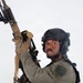 A uniformed security or military personnel member is posed against a white background holding a rifle upward. The individual is wearing full tactical gear including a ballistic helmet, plate carrier vest, and a patch identifying 'MCAS Miramar SRT' (Special Reaction Team). The image appears to be a professional portrait or promotional photograph.
