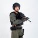 A male individual is posed against a plain white studio background wearing full tactical/law enforcement gear. He is holding a rifle with mounted accessories in a low-ready or patrol carry position. The image appears to be a professional equipment or personnel documentation photograph.