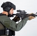 A tactical operator or law enforcement personnel is shown in a side-profile stance aiming an AR-15/M4-style rifle. The individual is equipped with full tactical gear including a ballistic helmet, body armor, and communications equipment. The image appears to be a professional studio or product photograph taken against a plain white background.