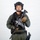 MCAS Marines pose for content 2026 A male individual in full tactical/military gear is posed against a plain white background in what appears to be a professional studio photograph. He is wearing olive drab fatigues, a black tactical vest, and a black ballistic helmet with communications equipment. He is holding an assault rifle with accessories across his chest in a ready/display position.