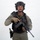 MCAS Marines pose for content 2026 A male individual in full tactical/military gear is posed against a plain white background. He is equipped with a rifle, tactical vest, helmet with night-vision mount, and sidearm holster. The image appears to be a professional or studio-style portrait photograph.