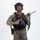 MCAS Marines pose for content 2026 A young male individual is photographed against a plain white studio background in full tactical gear. He is wearing olive/ranger green uniform with black plate carrier vest, ballistic helmet with accessories, and is holding a short-barreled rifle with optics. The image appears to be a professional equipment or catalog-style photograph.