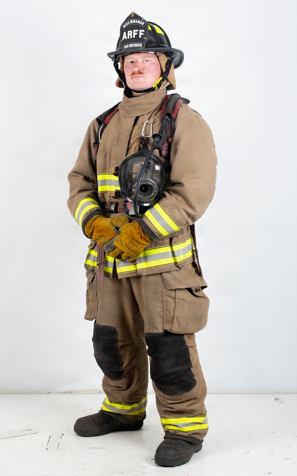 A firefighter in full personal protective equipment (PPE) stands in a formal portrait pose against a white background. The individual is wearing ARFF (Aircraft Rescue and Firefighting) gear from MCAS Miramar, identified as a Lead Firefighter. They are holding a breathing apparatus face mask and have SCBA (Self-Contained Breathing Apparatus) equipment on their back.