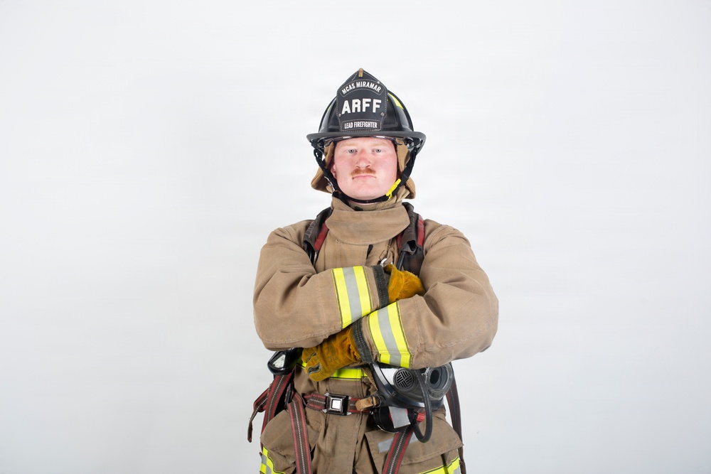 A firefighter in full turnout gear poses with arms crossed against a plain white background. The helmet is black and clearly marked 'ARFF' and 'MCAS MIRAMAR' with the designation 'LEAD FIREFIGHTER'. The image appears to be a professional portrait or official photo.