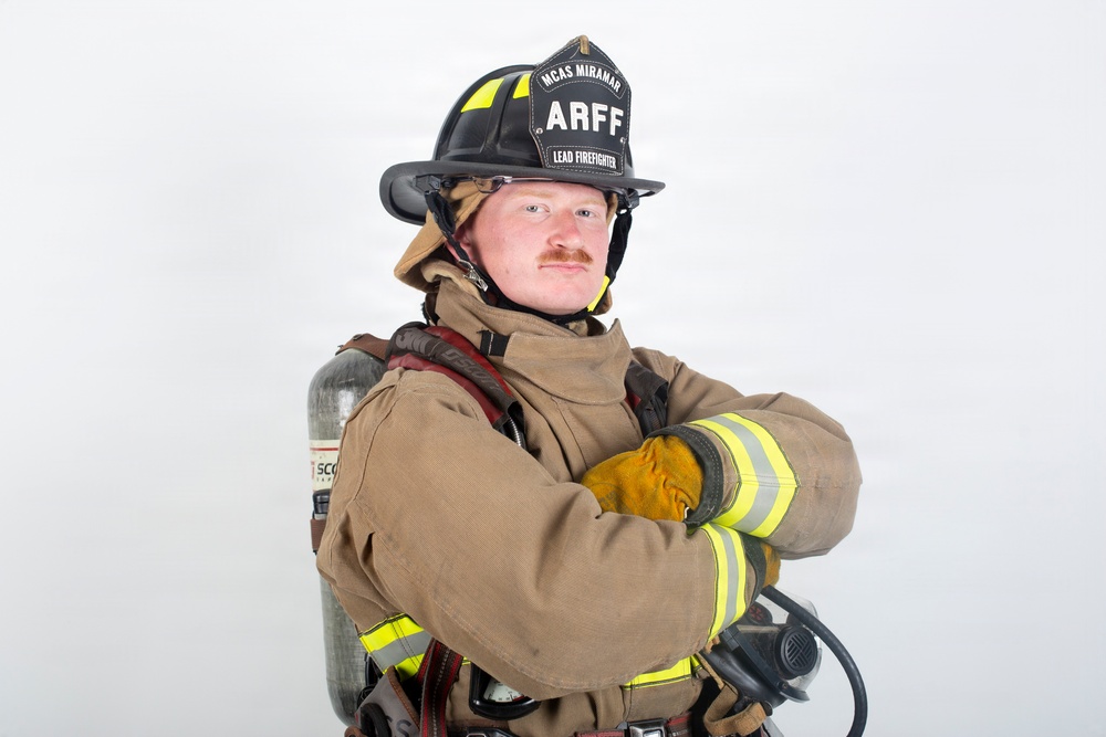 A firefighter in full turnout gear poses against a white background with arms crossed. The helmet identifies them as a 'Lead Firefighter' with 'ARFF' (Aircraft Rescue and Firefighting) designation at 'MCAS Miramar'. The subject is equipped with a Scott SCBA (Self-Contained Breathing Apparatus) tank on their back.