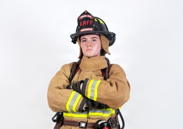 A firefighter in full personal protective equipment (PPE) stands in a confident pose with arms crossed against a plain white background. The individual is wearing tan/gold turnout gear with high-visibility yellow-green reflective striping, a black firefighting helmet labeled 'ARFF' and 'FIREFIGHTER' with unit designation 'MWSS-379'. The image appears to be a professional portrait or official documentation photograph.