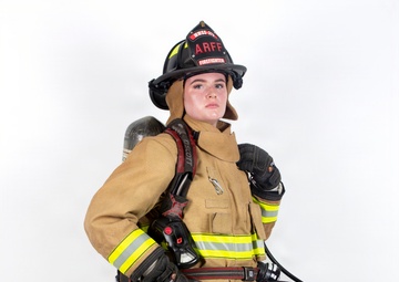 A firefighter in full turnout gear is posed against a white studio background. The individual is wearing complete personal protective equipment including a black helmet labeled 'ARFF' and 'FIREFIGHTER', a tan/gold bunker suit with high-visibility yellow reflective striping, and is carrying an SCBA (Self-Contained Breathing Apparatus) on their back. The image appears to be a professional portrait or equipment showcase photograph.