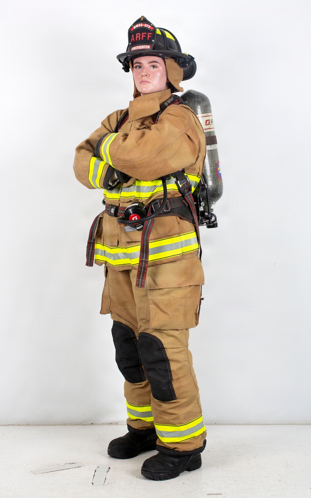 A firefighter in full personal protective equipment (PPE) stands in a posed position against a white studio background. The individual is wearing ARFF (Aircraft Rescue and Firefighting) gear, including a black helmet labeled 'ARFF FIREFIGHTER' with the designation 'HWSS-373', a tan turnout suit with yellow/lime reflective striping, and an SCBA (Self-Contained Breathing Apparatus) tank on their back. The image appears to be a professional or promotional photograph showcasing the complete firefighting ensemble.