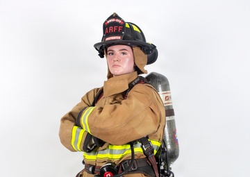 A firefighter in full personal protective equipment (PPE) stands in a posed position against a white studio background. The individual is wearing ARFF (Aircraft Rescue and Firefighting) gear, including a black helmet labeled 'ARFF FIREFIGHTER' with the designation 'HWSS-373', a tan turnout suit with yellow/lime reflective striping, and an SCBA (Self-Contained Breathing Apparatus) tank on their back. The image appears to be a professional or promotional photograph showcasing the complete firefighting ensemble.