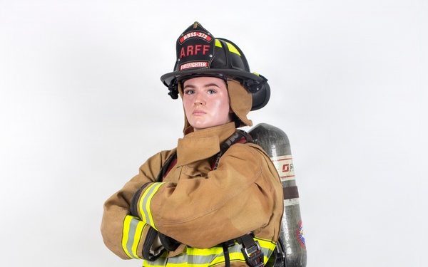A firefighter in full personal protective equipment (PPE) stands in a posed position against a white studio background. The individual is wearing ARFF (Aircraft Rescue and Firefighting) gear, including a black helmet labeled 'ARFF FIREFIGHTER' with the designation 'HWSS-373', a tan turnout suit with yellow/lime reflective striping, and an SCBA (Self-Contained Breathing Apparatus) tank on their back. The image appears to be a professional or promotional photograph showcasing the complete firefighting ensemble.