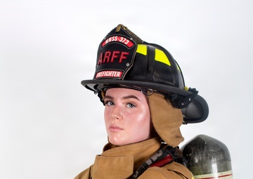 A firefighter in full turnout gear poses for a professional portrait against a white background. The individual is wearing an ARFF (Aircraft Rescue and Firefighting) helmet marked 'MWSS-373' and 'FIREFIGHTER,' with arms crossed in a confident stance. Full personal protective equipment is visible including a SCBA (Self-Contained Breathing Apparatus) tank on the back.