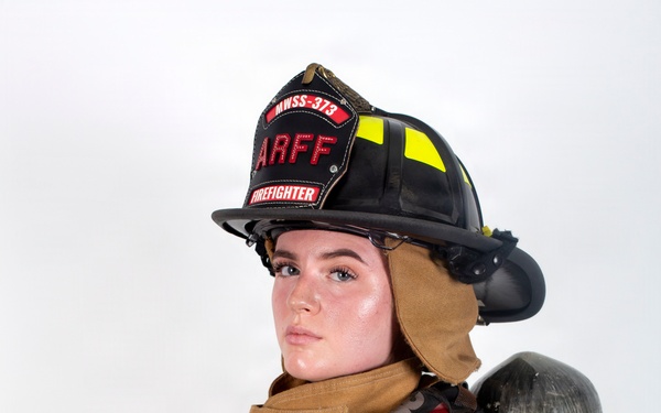 A firefighter in full turnout gear poses for a professional portrait against a white background. The individual is wearing an ARFF (Aircraft Rescue and Firefighting) helmet marked 'MWSS-373' and 'FIREFIGHTER,' with arms crossed in a confident stance. Full personal protective equipment is visible including a SCBA (Self-Contained Breathing Apparatus) tank on the back.