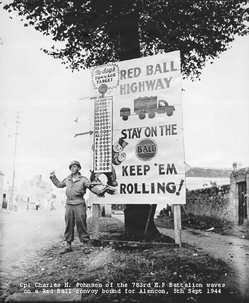 A black-and-white World War II photograph dated 5th September 1944, showing Corporal Charles H. Johnson of the 783rd Military Police Battalion standing beside a large Red Ball Highway promotional sign in Alençon, France. The sign encourages convoy drivers to meet tonnage targets and keep supplies moving toward Allied forces. The image is a well-documented historical record of the famous Red Ball Express logistics operation.