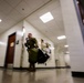 A soldier in military camouflage uniform is moving rapidly through an indoor corridor, carrying large duffel bags. The photo is taken from a low angle with motion blur, suggesting urgency or rapid movement. The setting appears to be a institutional building such as a school or government facility based on the hallway design.