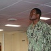 A U.S. Navy service member wearing the Navy Working Uniform (NWU) Type III in woodland digital camouflage pattern stands at attention or in a formal posture indoors. The uniform displays 'U.S. NAVY' chest tape, a name tape reading 'TURNER', an American flag patch on the right sleeve, and what appears to be an Ensign (O-1) rank insignia. The setting appears to be a military facility or command building.