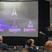 A military officer in combat uniform is presenting a briefing about the United States Space Force organizational structure at what appears to be a Marriott conference venue. The presentation slide displays the Space Force logo and three subordinate commands: Combat Forces Command (CFC), Space Training and Readiness Command (STARCOM), and Space Systems Command (SSC). An audience of civilians and officials is seated facing the presenter.