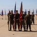 A U.S. Marine Corps color guard stands at attention on a military airfield tarmac during a formal ceremony. The central group holds the American flag and what appears to be a Marine Corps unit guidon, surrounded by rows of state and unit flags. Military helicopters, including what appears to be CH-53s and V-22 Ospreys, are visible in the background.