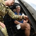 A U.S. Army soldier with the name tape 'EISELE' is assisting a civilian man seated inside what appears to be a military helicopter cockpit. The soldier, wearing Operational Camouflage Pattern (OCP) uniform with 'U.S. ARMY' tape visible, appears to be orienting or briefing the civilian on the aircraft's interior. The setting suggests a public demonstration, airshow, or familiarization event.