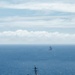An aerial or elevated photograph showing two naval vessels underway on open ocean. The foreground vessel is a US Navy Arleigh Burke-class guided-missile destroyer bearing the hull number '101' on its bow. A second, larger vessel is visible in the distant background near the horizon.