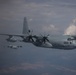 The image shows multiple military turboprop transport aircraft flying in formation at altitude. The lead aircraft, marked with the number '065', is a C-130 Hercules variant in a gray military paint scheme. At least two additional C-130-type aircraft are visible in the background flying in loose formation.