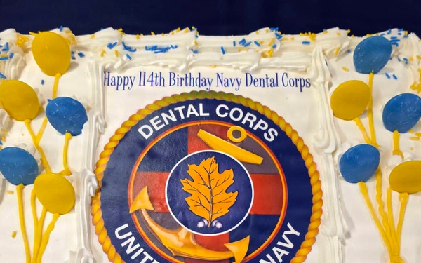 A rectangular sheet cake with white frosting celebrating the 114th Birthday of the United States Navy Dental Corps. The cake features the official Navy Dental Corps seal in the center and is decorated with blue and gold balloon-shaped candy decorations and colored sprinkles. The inscription reads 'Happy 114th Birthday Navy Dental Corps' above the emblem.