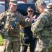 Three individuals are engaged in a conversation outdoors on a grassy area. Two are wearing U.S. Army OCP (Operational Camouflage Pattern) uniforms with tactical gear, while a third individual wears black tactical clothing with a holstered sidearm. The leftmost soldier has a visible name tape reading 'CANNON' and wears a rank insignia consistent with a Lieutenant Colonel (oak leaf cluster).