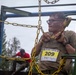 A participant in the 'XIV Bieg Tygrysa' (XIV Tiger Run) obstacle race is navigating a chain-based climbing structure, wearing bib number 209 written both on their race bib and on their cheek. The competitor appears wet and muddy, consistent with a tough mudder-style obstacle course event. A second participant in a red shirt is visible in the background on the same structure.